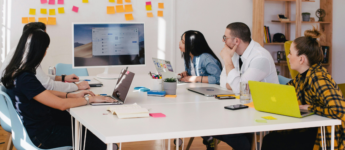 Personen sitzen am Tisch und schauen auf einen Bildschirm